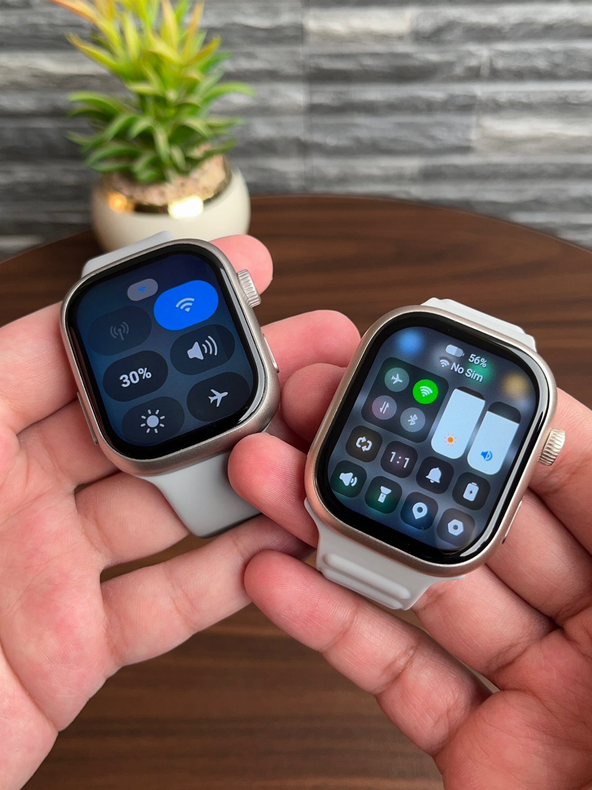 Two silver smartwatches with grey straps held over a wooden table.