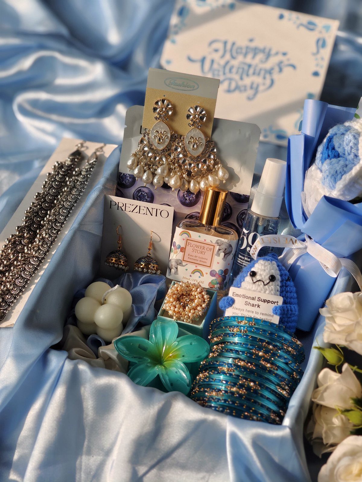 Gift box with blue satin lining containing jewelry, perfume, and Valentine's Day card.
