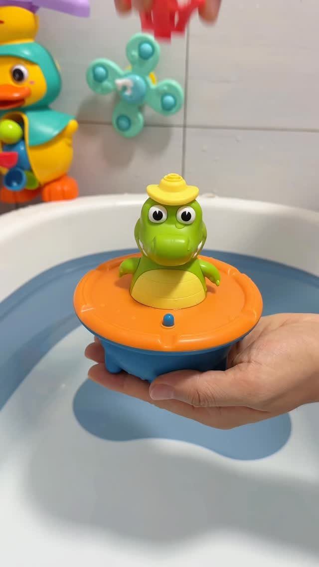 Green crocodile bath toy on a floating base held over a white bathtub.
