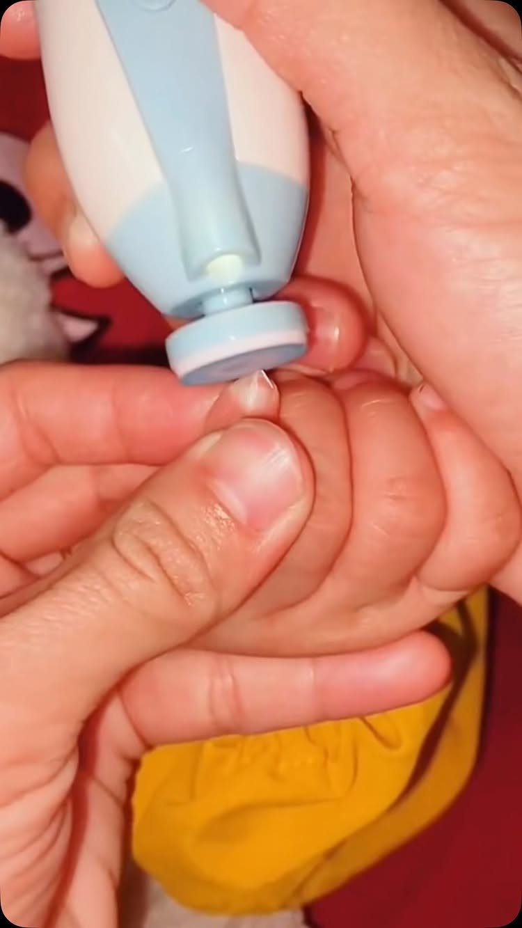Electric baby nail trimmer being used on a baby's small fingernail.