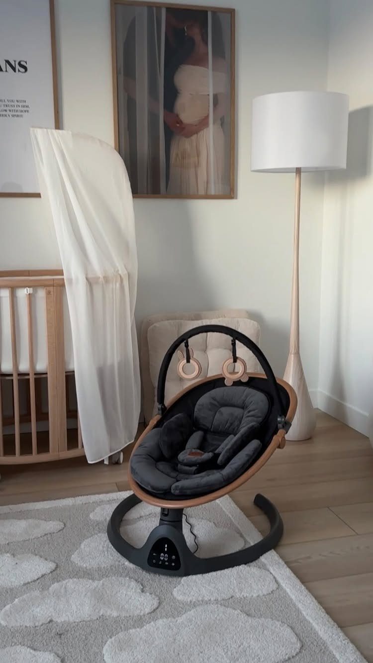 Modern baby swing with grey seat and wooden frame in a neutral nursery.