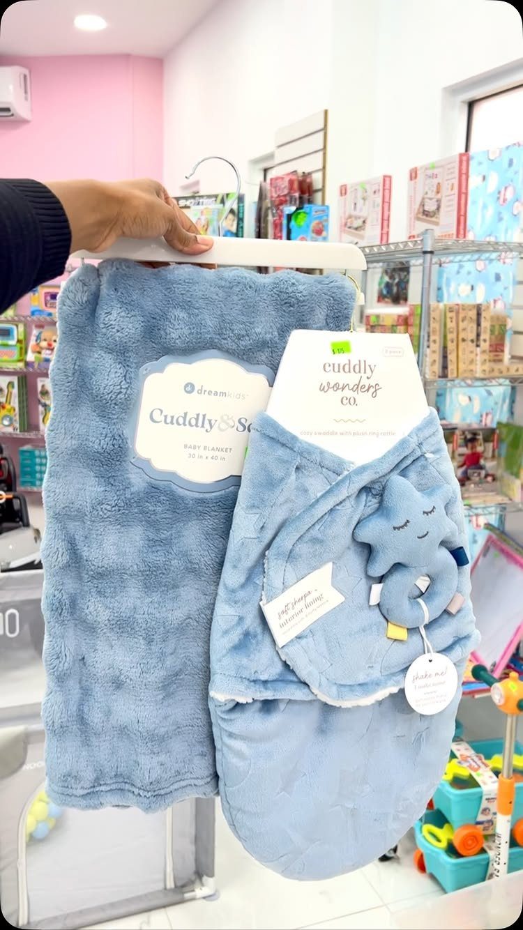 Two light blue plush baby blankets, one with a star plush toy, in store.