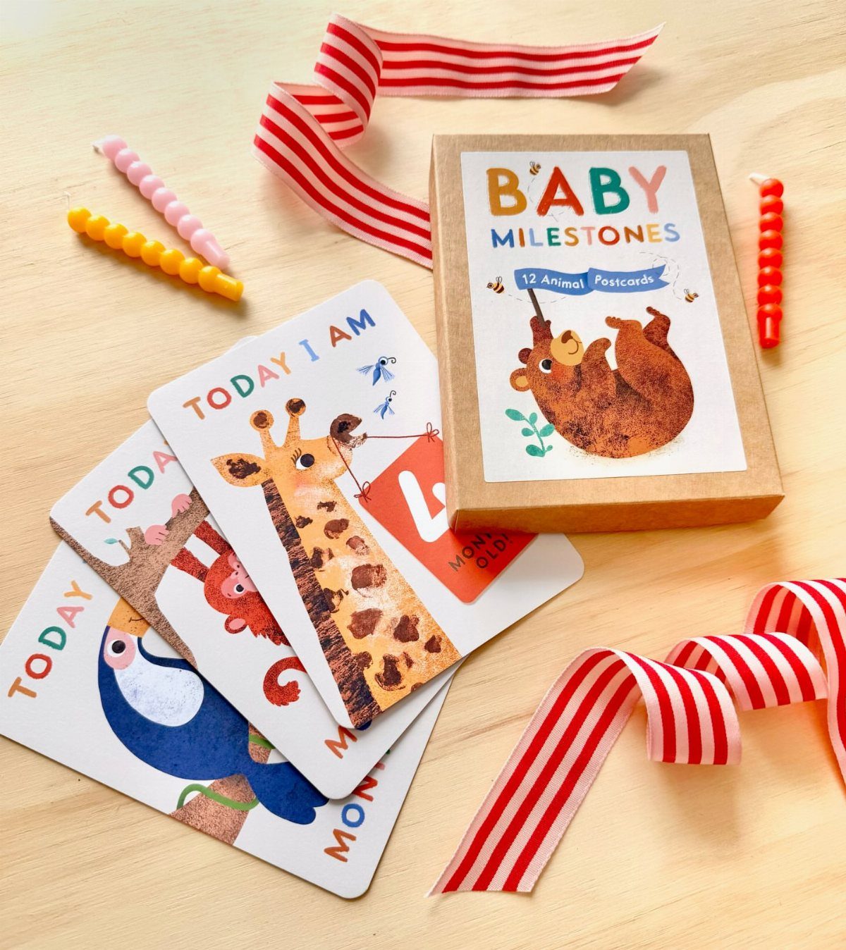 Baby milestone cards with animal illustrations and a matching gift box on wood.