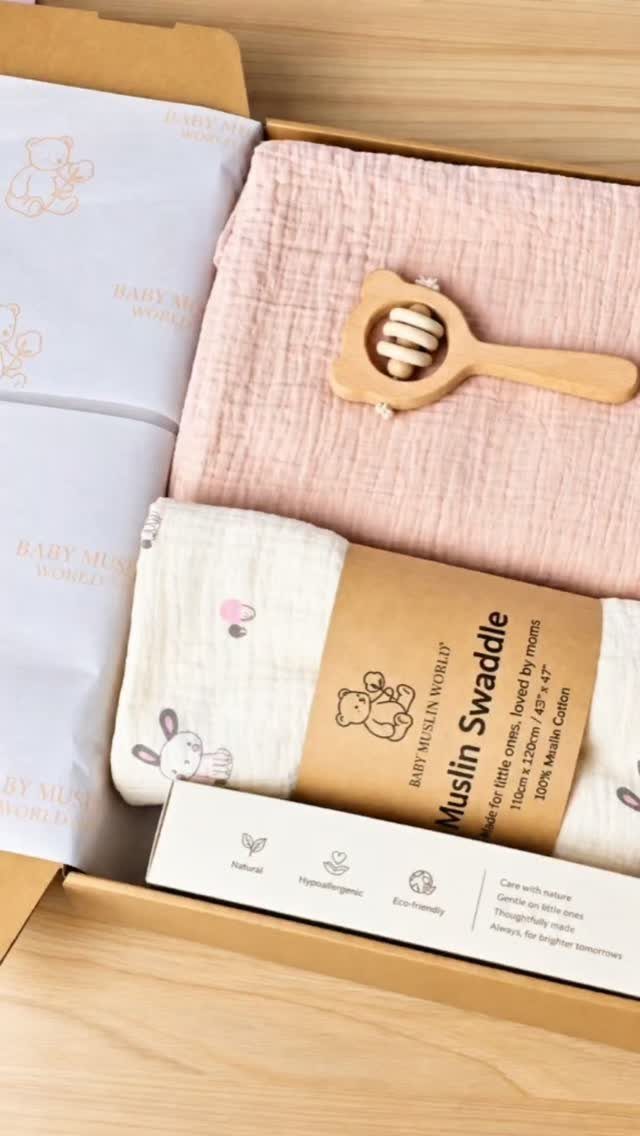 Muslin swaddles and a wooden teether arranged inside a cardboard gift box.