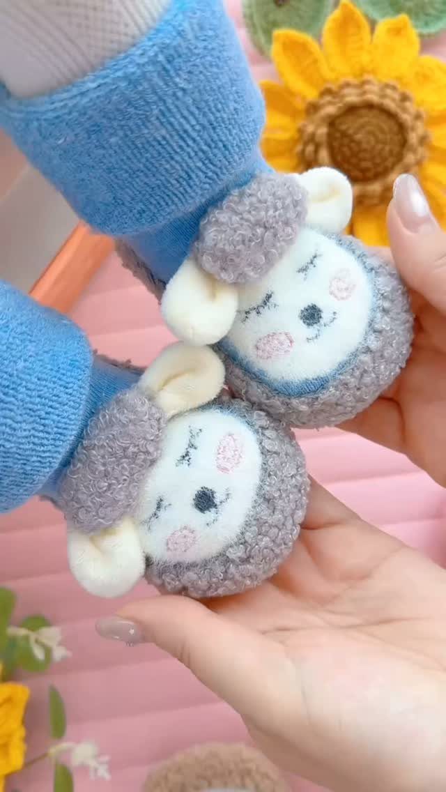 Blue baby socks with plush sheep faces on the toes held by hands.
