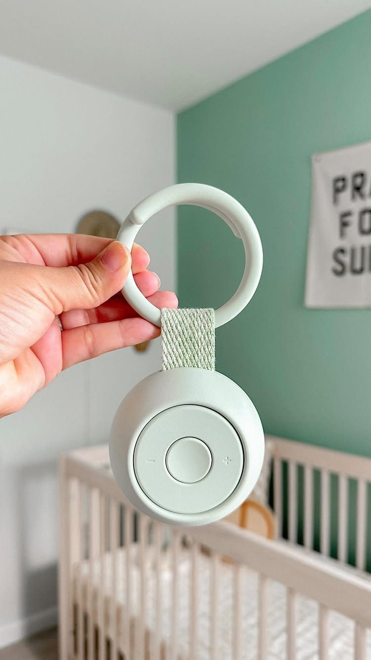 Mint-green portable baby sound machine held in front of a white nursery crib.