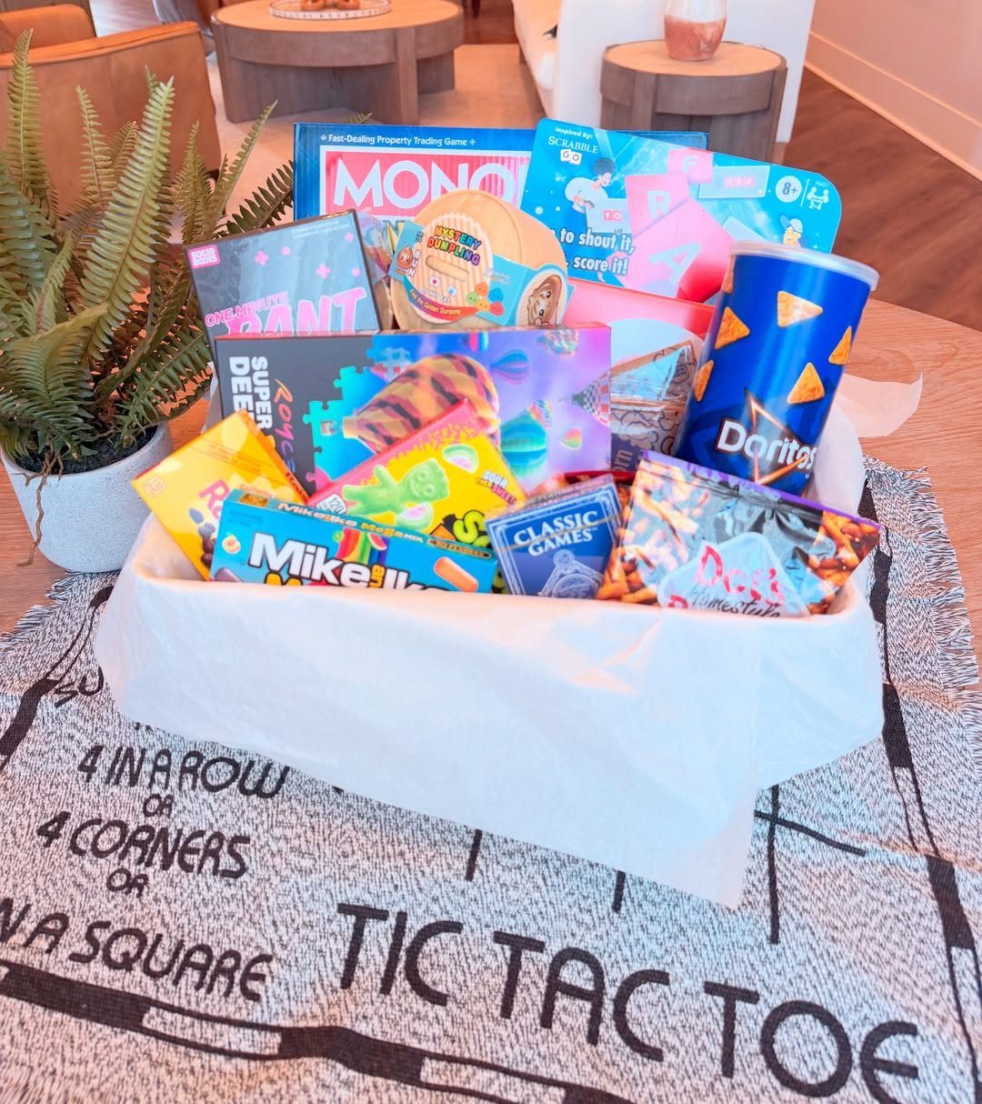 Board game gift basket with snacks and games on a Tic Tac Toe rug.