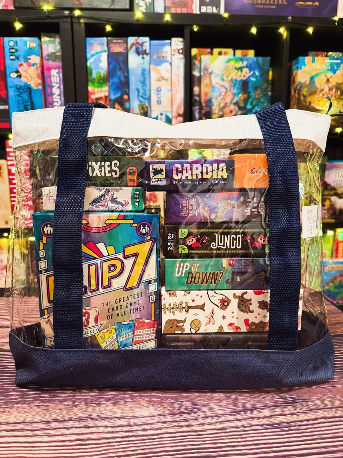 Clear plastic tote bag filled with various colorful board games on wooden surface