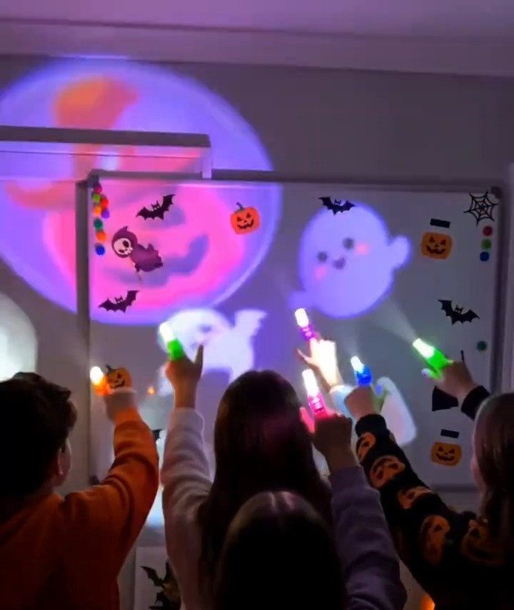 Children holding colorful glow sticks in front of a Halloween themed projection.