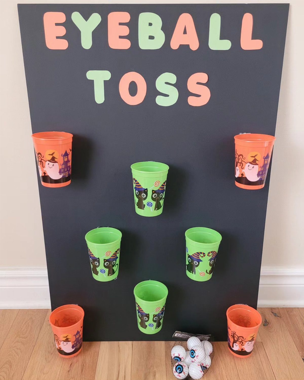 Eyeball toss game with colorful plastic cups attached to a black board.