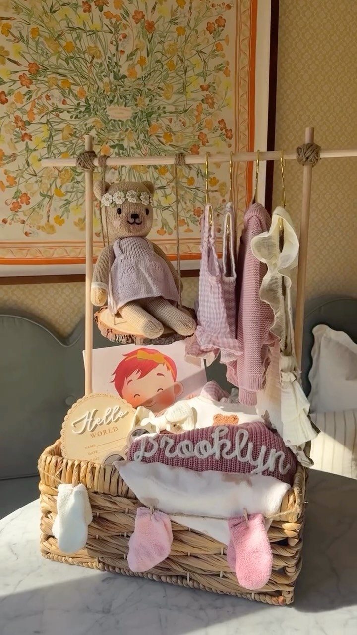 Wicker baby shower gift basket with pink clothes, socks, and a teddy bear.