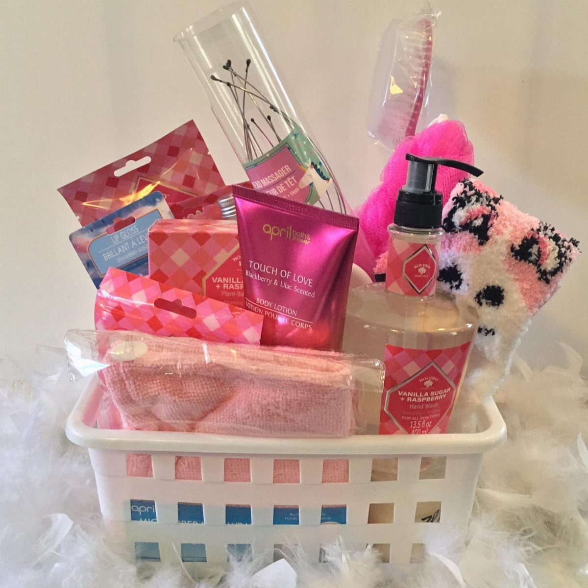 White basket filled with pink spa products, lotion, and towels on white fluff.