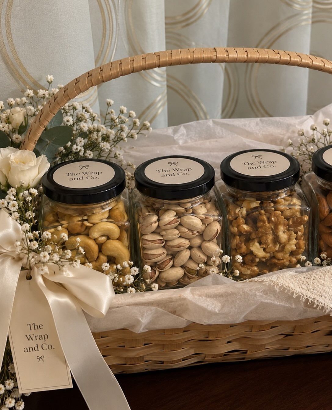 Woven gift basket with glass jars of nuts, white flowers, and cream ribbon.