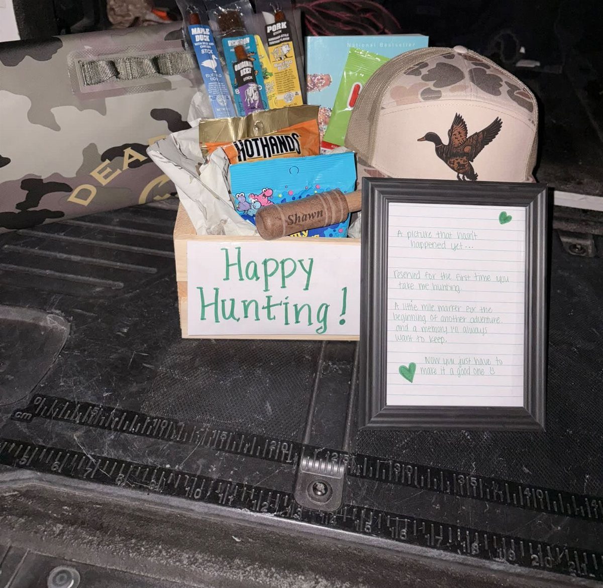 Hunting gift basket in a wooden crate with a camouflage duck hat and snacks.