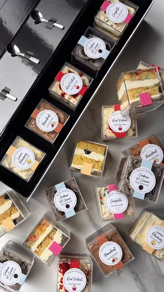 Layered cake slices in small clear plastic boxes with ribbons and labels.
