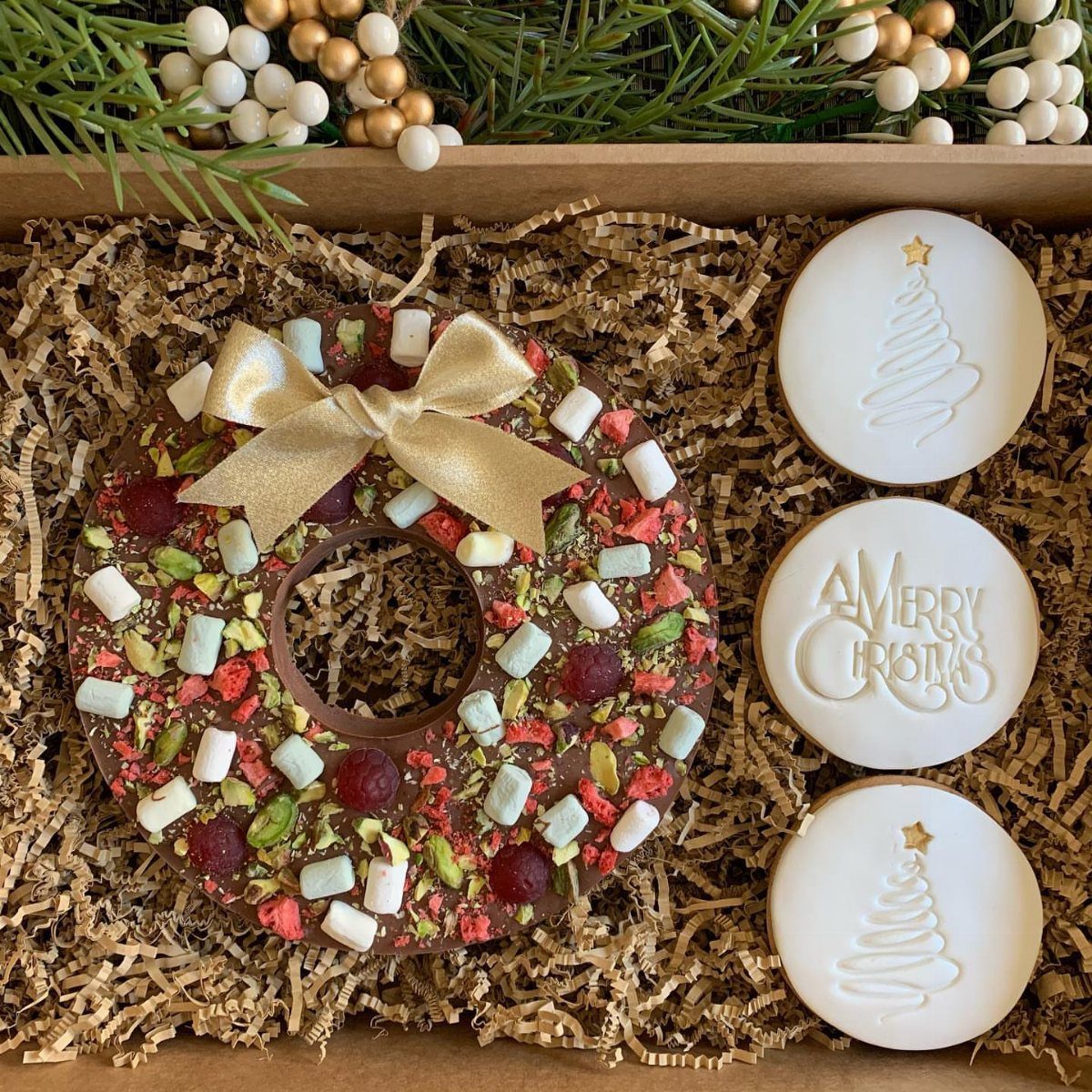 Chocolate wreath cookie with toppings and white frosted Christmas cookies in a gift box