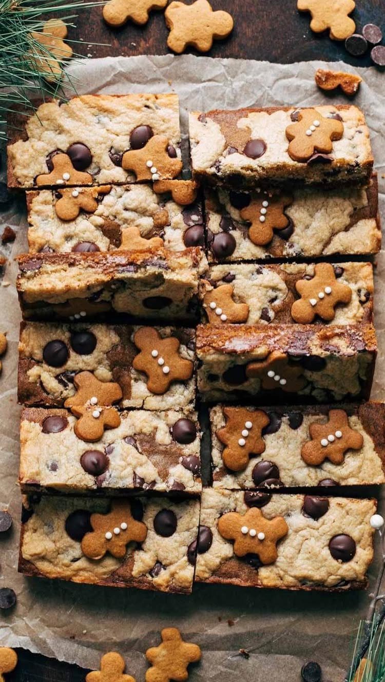 Gingerbread chocolate chip cookie bars topped with small gingerbread men on parchment paper.
