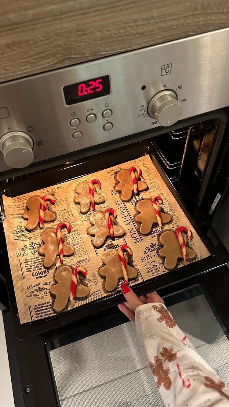 Gingerbread man cookies with candy canes on a baking tray inside an oven.