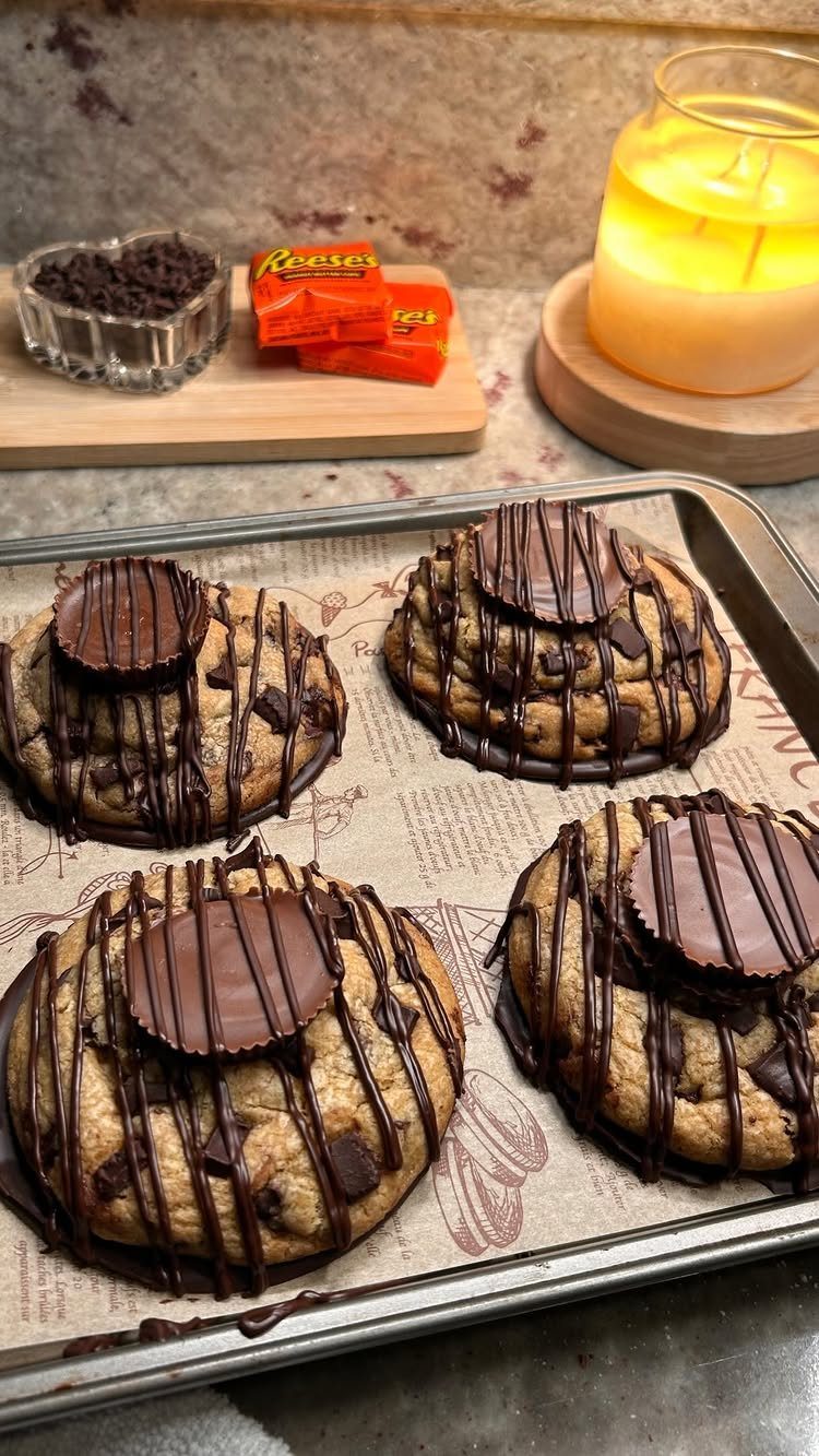Chocolate chip cookies topped with peanut butter cups and chocolate drizzle on a tray.