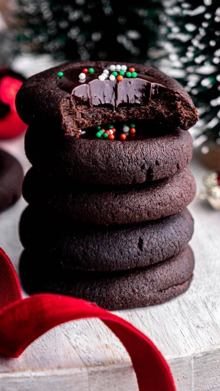 Stack of chocolate thumbprint cookies with festive sprinkles and a red ribbon.