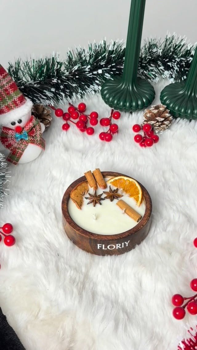 White candle in a wooden bowl with cinnamon and orange slices on white fur