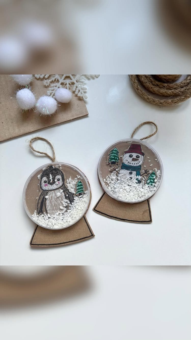 Two circular snow globe ornaments featuring a penguin and a snowman with faux snow.