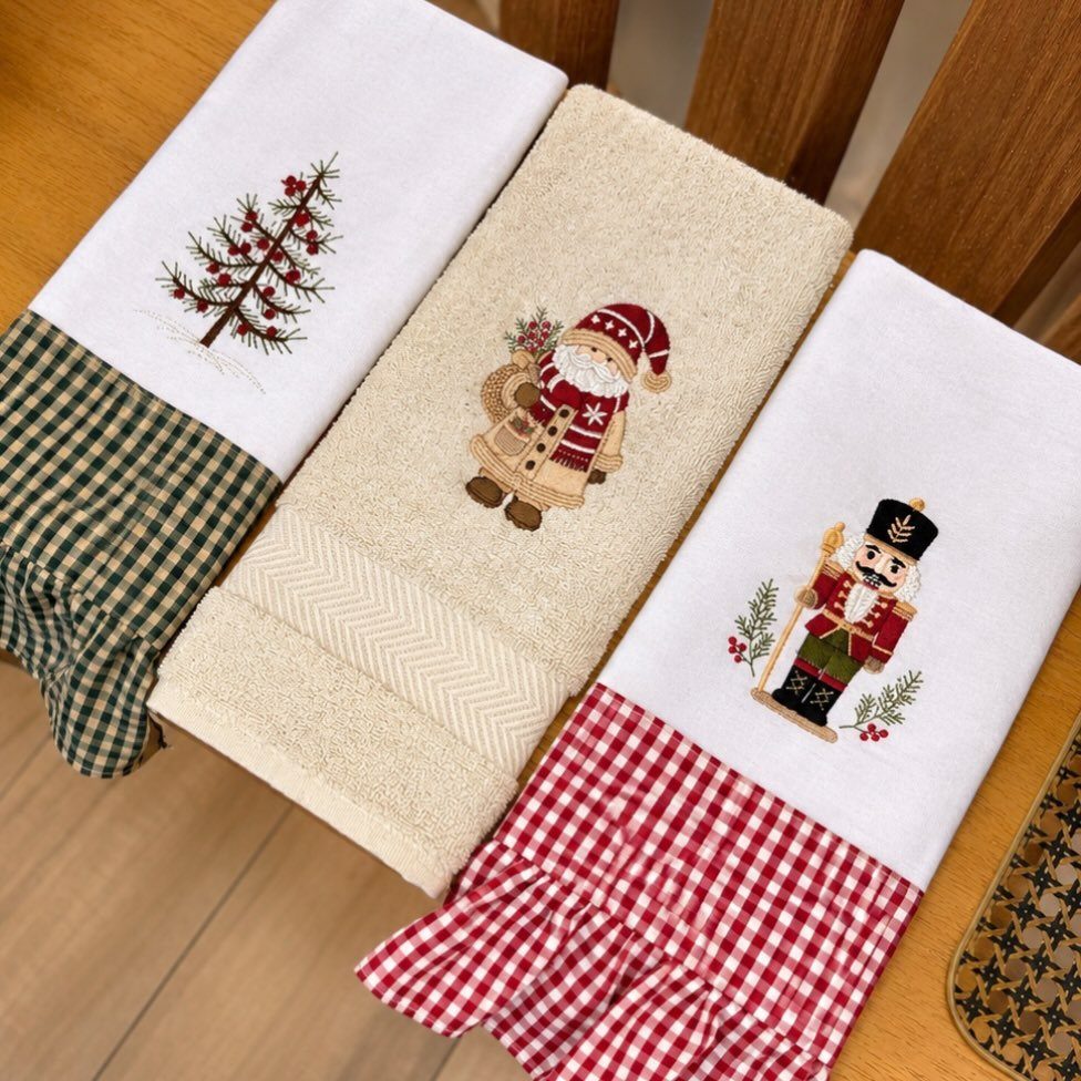 Three kitchen towels with embroidered Christmas tree, Santa, and nutcracker festive designs.