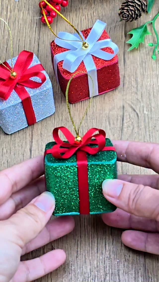 Glittery green gift ornament held by hands with red and silver ornaments nearby.