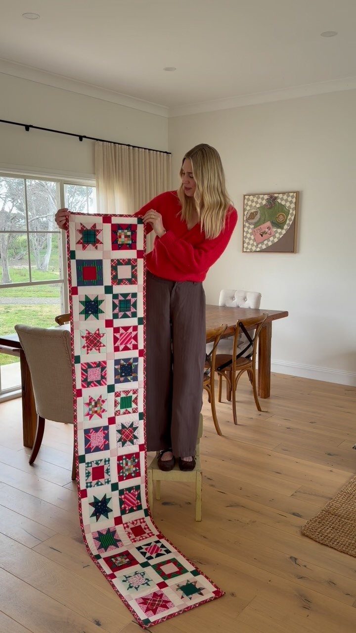 Woman holding a long handmade red and green patchwork Christmas quilt in a room