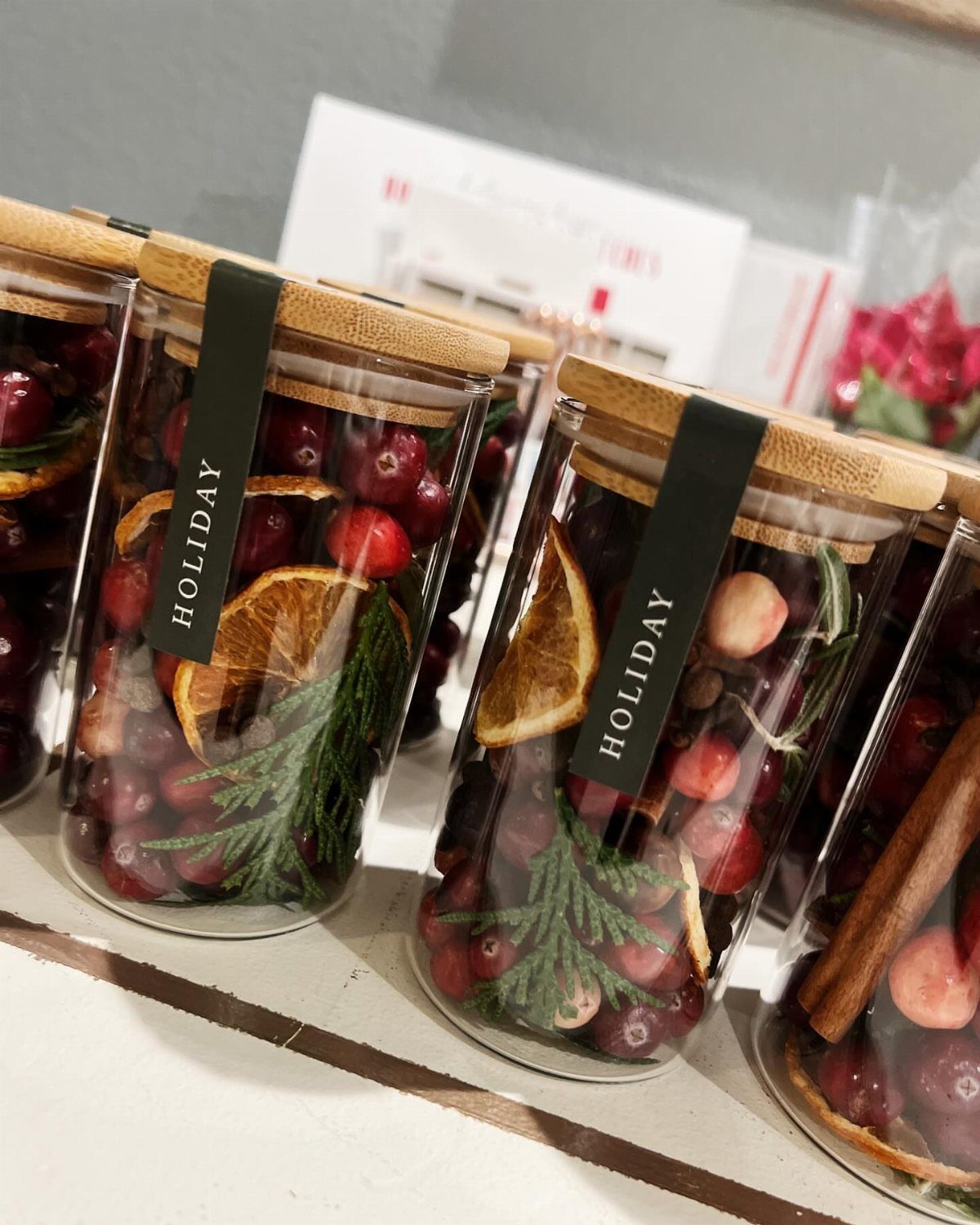 Glass jars filled with cranberries, dried oranges, and pine needles for holiday potpourri.
