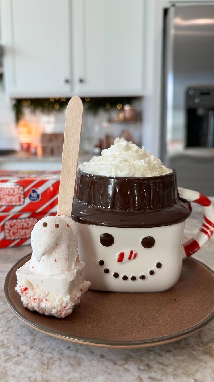 Snowman mug of hot chocolate with a peppermint chocolate stirring spoon on a plate