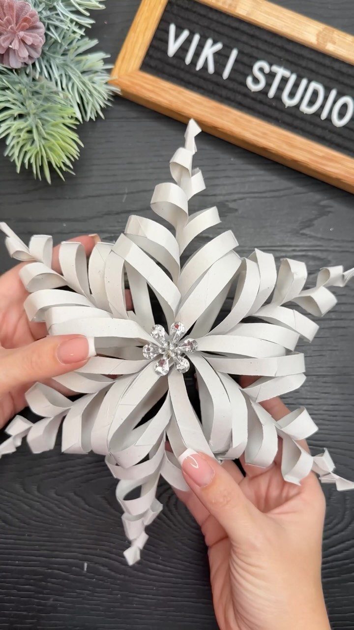 White paper snowflake ornament with a rhinestone center held by two hands