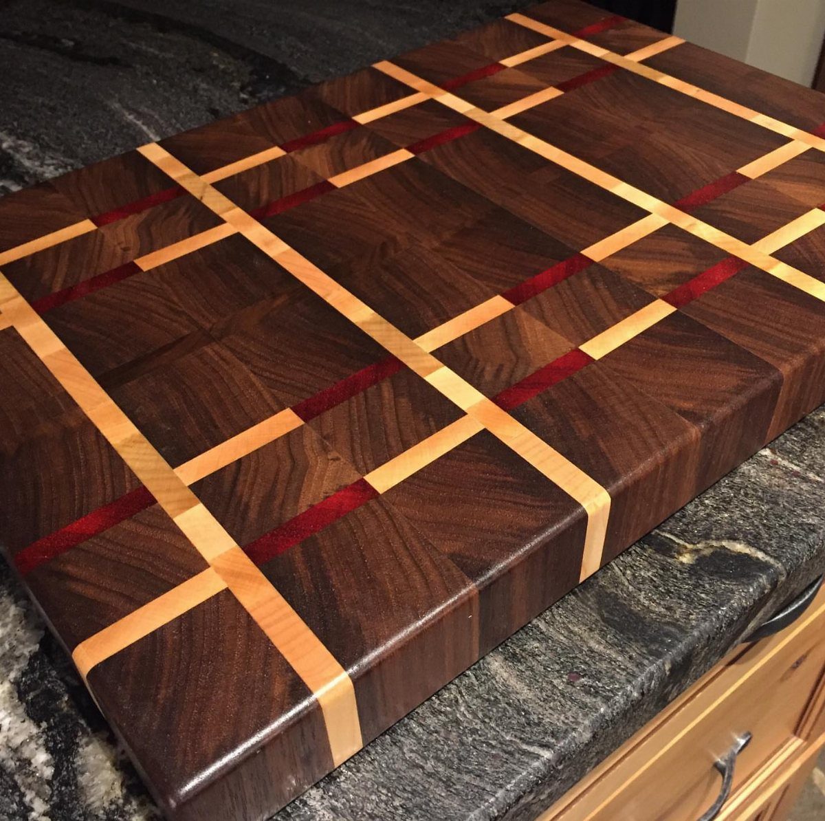 Wooden cutting board with a multicolored grid pattern on a granite countertop.