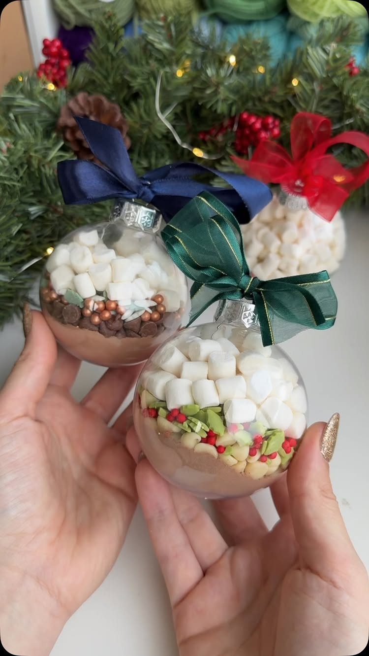 Hot cocoa mix in clear glass ornaments with ribbons held by two hands.