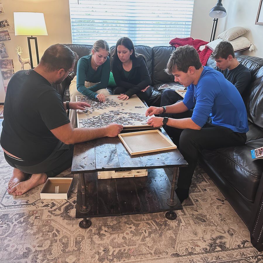 Family members working together to complete a large jigsaw puzzle on a coffee table