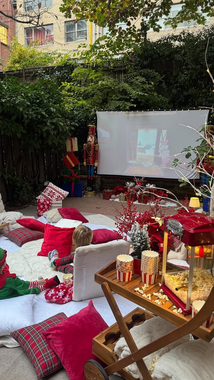 Outdoor movie theater setup with projector screen, red pillows, and popcorn cart.