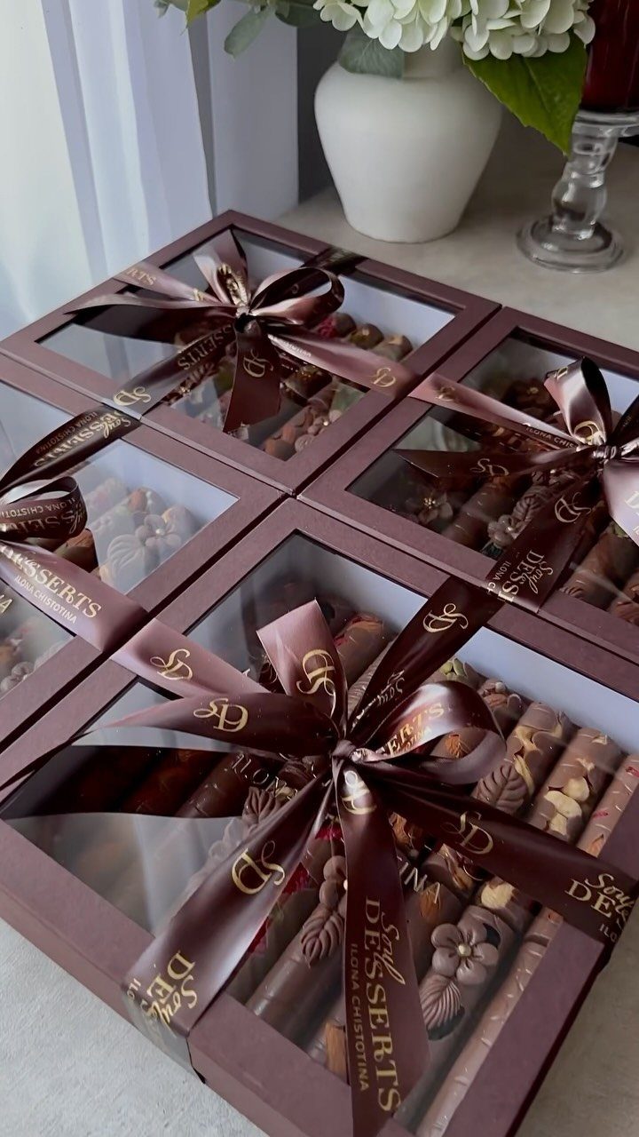 Four brown gift boxes filled with assorted chocolates, tied with brown satin ribbons.
