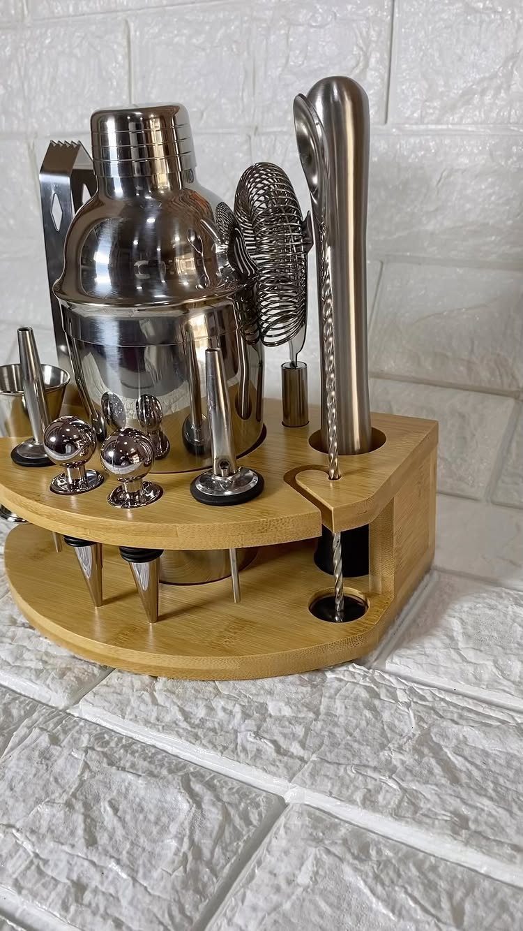 Stainless steel cocktail shaker set in a wooden stand against a white brick wall