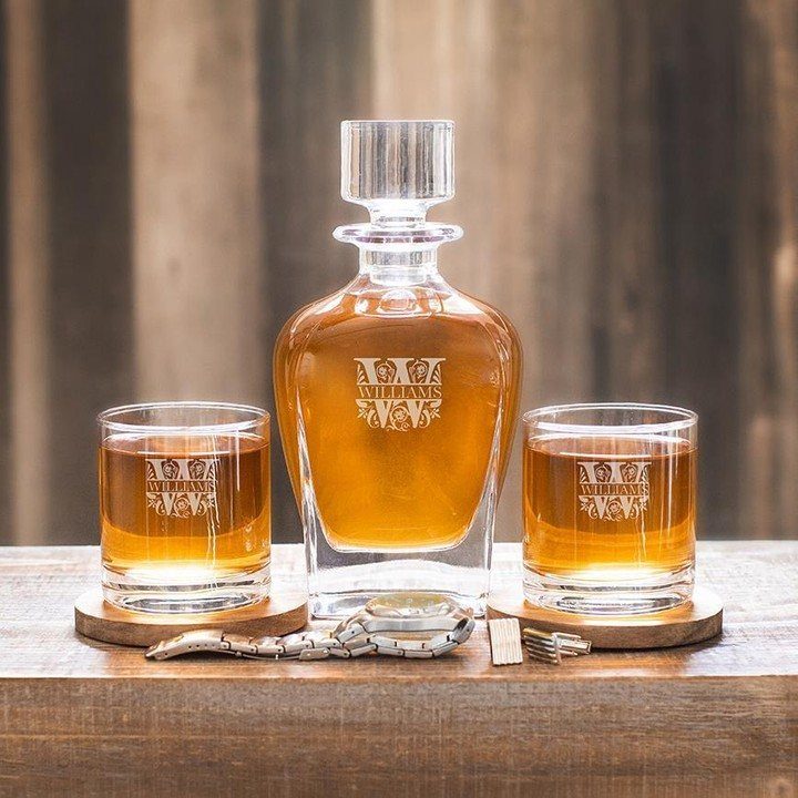 Engraved whiskey decanter and glasses set with a silver watch on wooden table