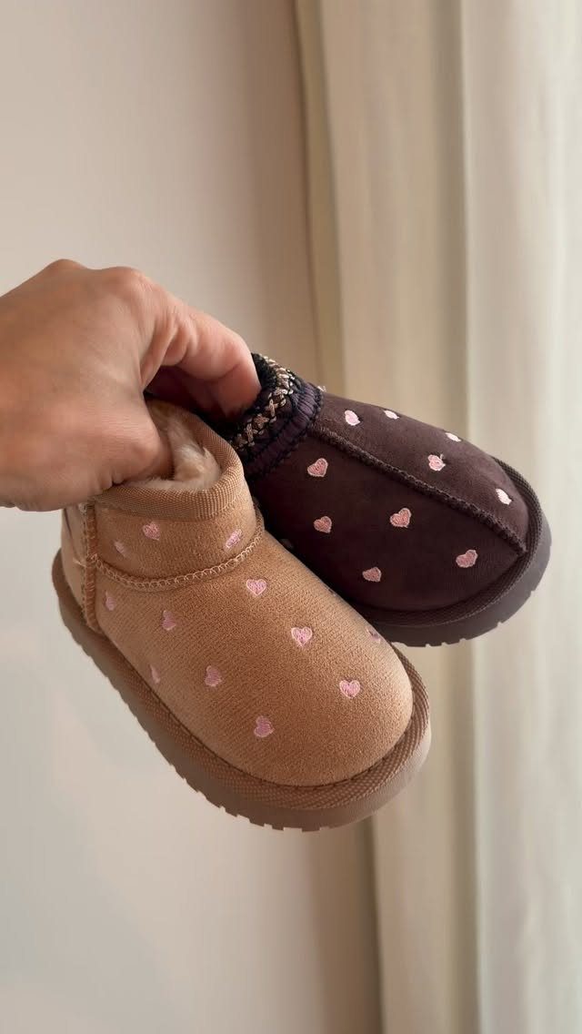 Two soft baby booties in tan and brown with pink heart patterns.