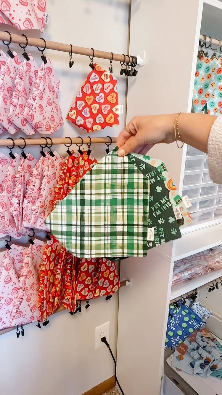 Green plaid fabric dog bandanas held by a hand with others hanging behind.