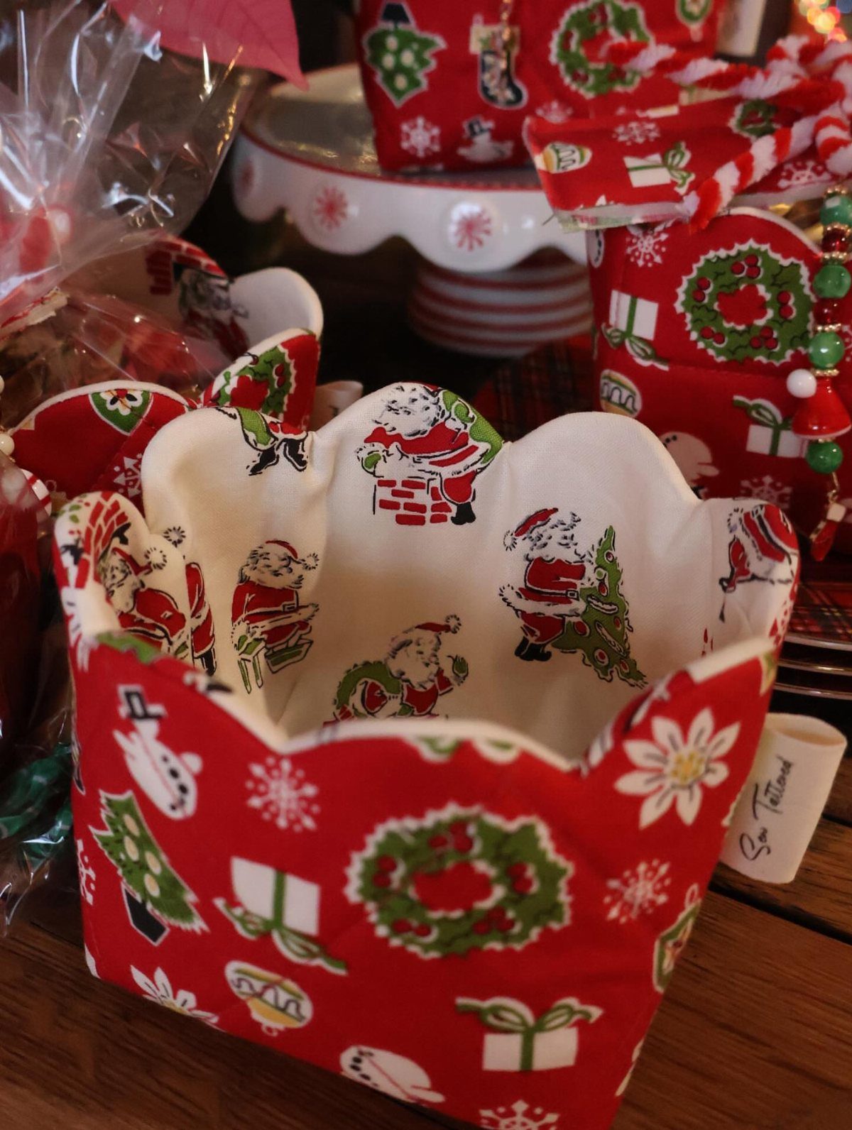 Red fabric Christmas basket with scalloped edges and Santa Claus patterns on wood.