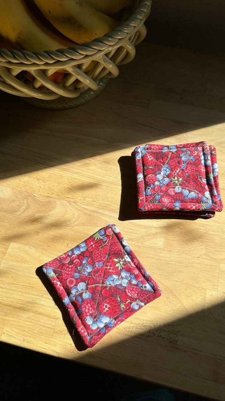 Quilted red and blue floral fabric coasters on a wooden table next to fruit.