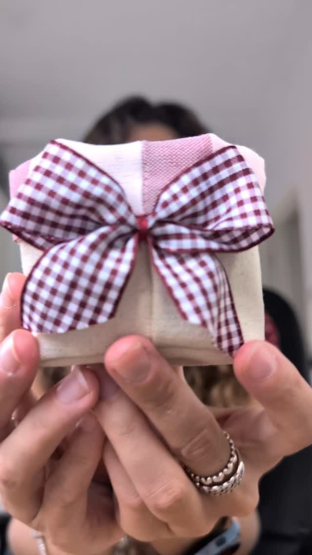 Handmade fabric gift box with a red gingham bow held by two hands.