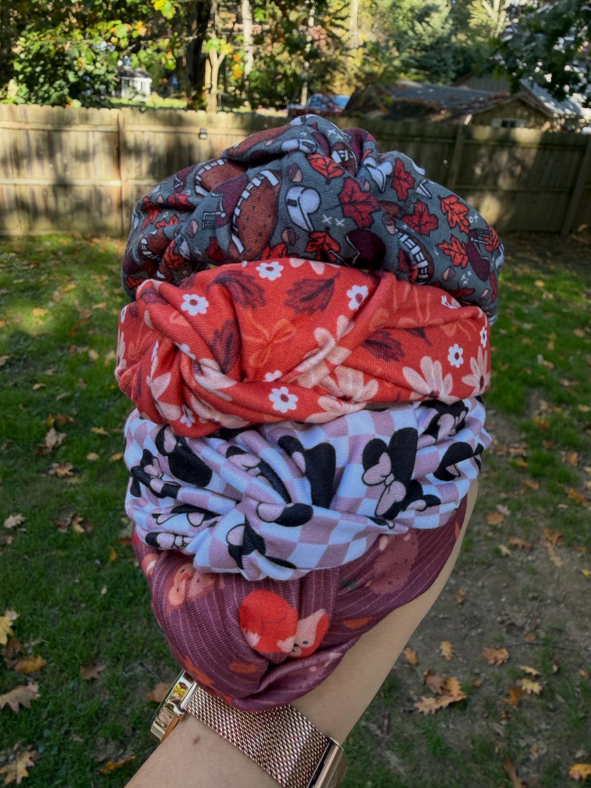 Four colorful patterned fabric twisted headbands stacked and held in a hand outdoors.