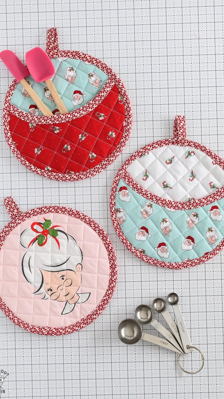 Three round quilted holiday pot holders and metal measuring spoons on a grid mat.