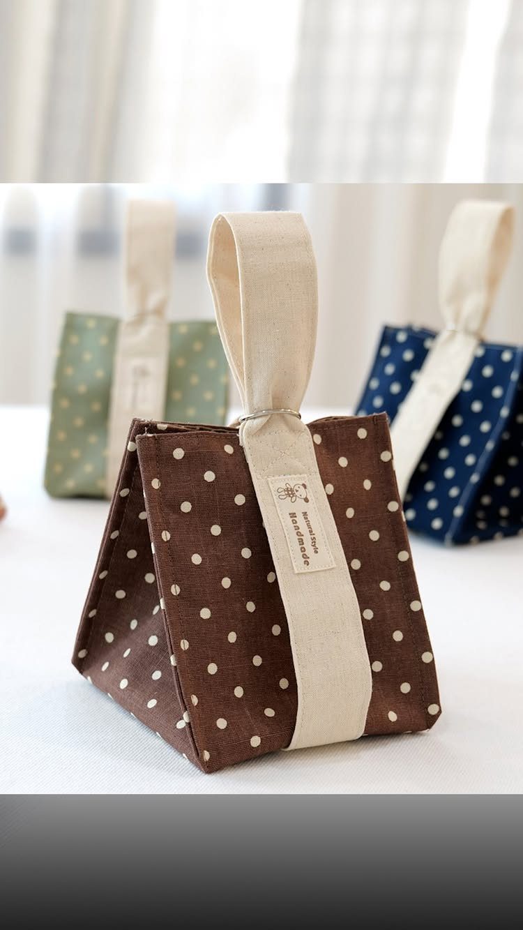 Small brown polka dot fabric gift bags with cream handles on white surface