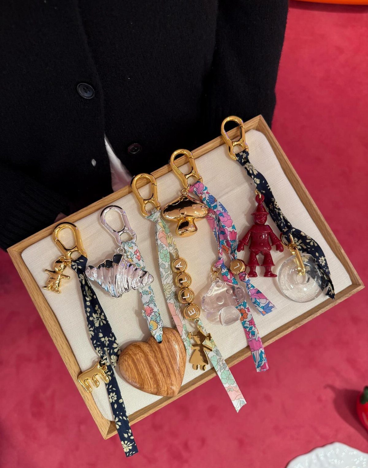 Colorful fabric keychains with various charms arranged on a light-colored wooden tray.