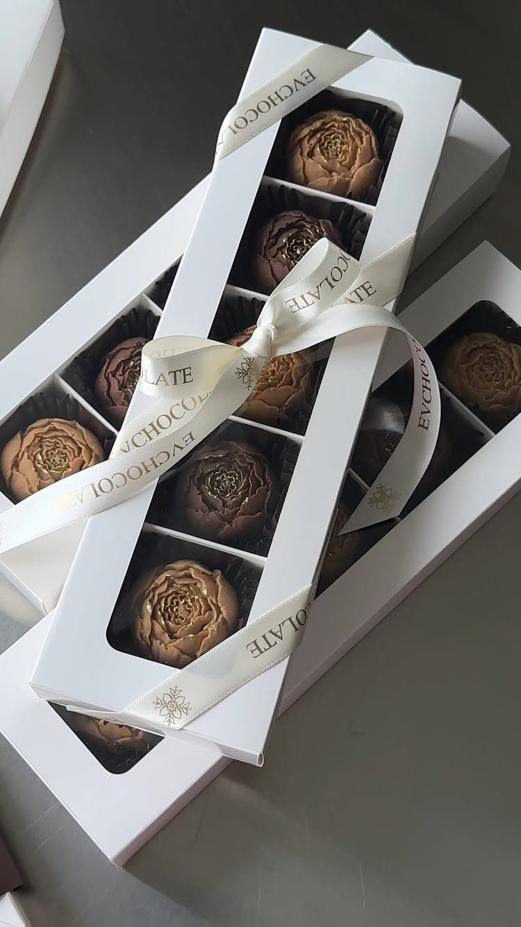 Gourmet rose-shaped chocolates in white gift boxes tied with a white ribbon.