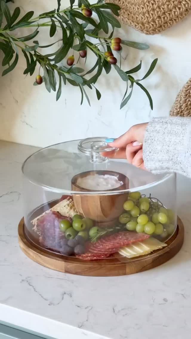 Cheese and charcuterie board under a glass dome on a marble countertop